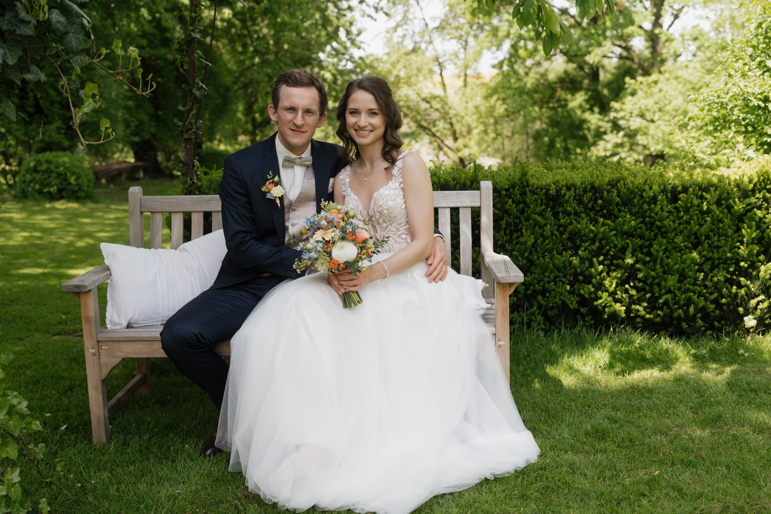 Braut und Bräutigam sitzen auf einer Bank im Park bei ihrer Hochzeit.